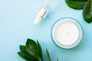 Natural cosmetic, cream jar with green leaves on blue.