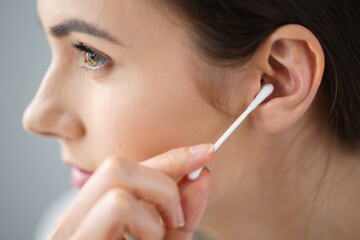 A young woman uses a cotton swab to clean her ear.