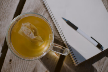 Top down view of a bagged tea cup and white paper journal open and a pen