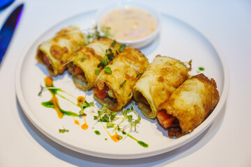 Pancake rolls stuffed with vegetables with sauce on a white round plate. 