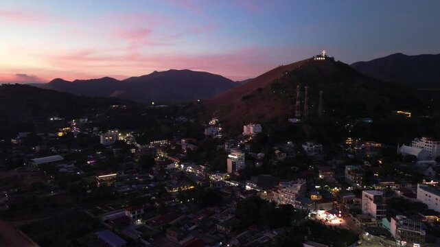 Coron town lights glow below Mount Tapyas at dusk with the hilltop cross visible against pink twilight clouds and Palawan mountain ridges