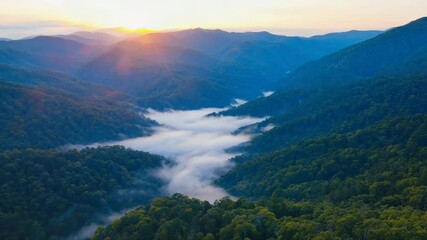 early morning foggy valley with sunlight breaking over green hills and blue mountains, perfect natural scenery for peaceful travel or relaxation videos