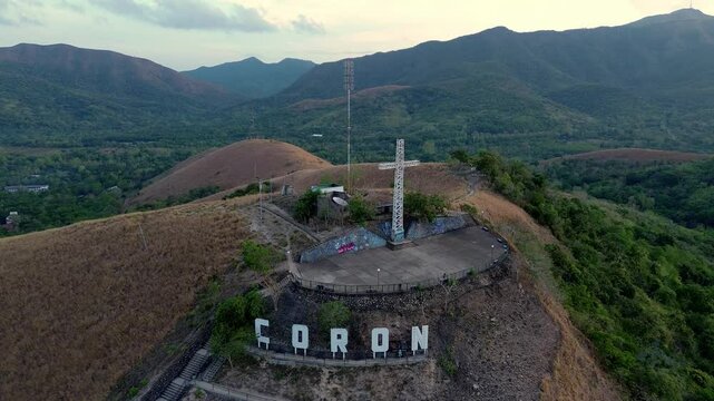 Mount Tapyas summit cross and viewing platform above Coron with dry grass slopes green Palawan hills and mountain valleys in morning light