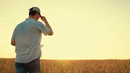 Farmer with computer tablet evaluates wheat sprouts in field, sun. Technology, agriculture business. Farmer, businessman working on field with digital tablet agriculture. Grow Ecologically clean grain