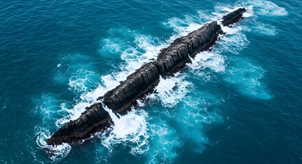 Aerial view of rocky outcrop in ocean with waves crashing against it on a sunny day