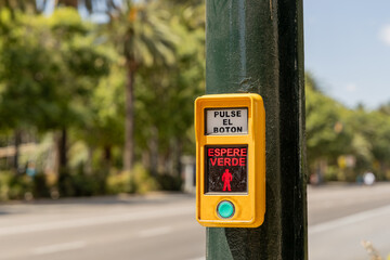  Pedestrian crossing button with instructions in Spanish, surrounded by palm trees and urban...