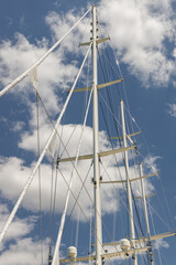 Tall white sailing mast against a bright blue sky with fluffy clouds, showcasing nautical elements...