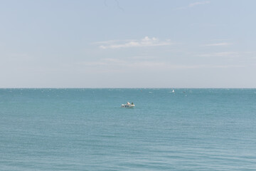 Fototapeta premium Small boat with two people sailing on calm blue waters under a clear sky, evoking a sense of summer vacation and relaxation by the sea