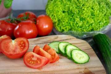 Sliced cucumber and tomatoes on a wooden board with a knife, surrounded by fresh vegetables like tomatoes and lettuce. Ideal for healthy eating, cooking content, vegan recipes, or kitchen visuals.