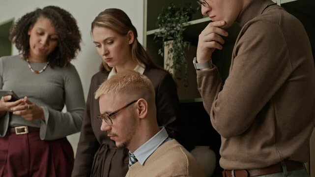 Side view of multiethnic team of office workers discussing problem looking at laptop screen while brainstorming during daily meeting at workplace