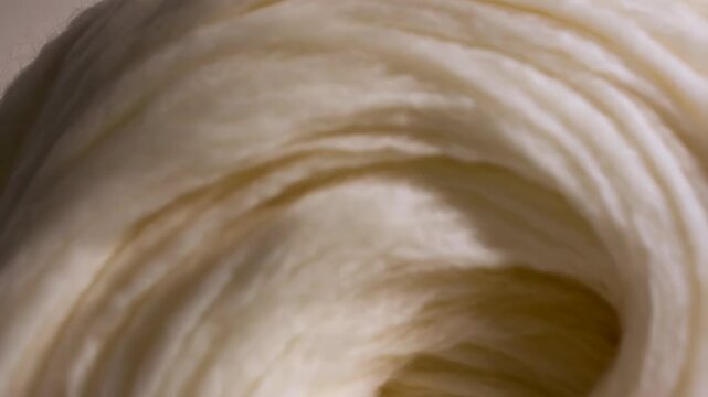 Close-up shot of a soft, fluffy skein of creamy white merino wool, with smooth and silky fibers swirled in a circular pattern forming a soft and warm texture.