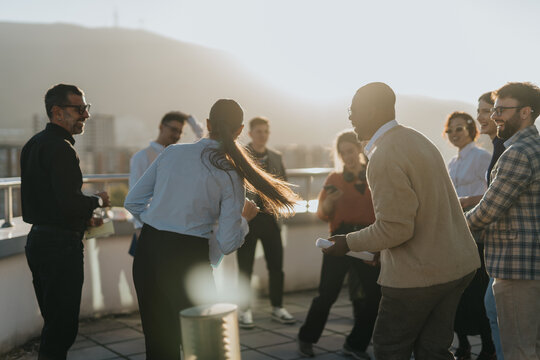 A diverse group of business people celebrate success on a high rooftop at sunset, enjoying music and dancing while sharing joyful moments together against a beautiful cityscape backdrop. - Powered by Adobe
