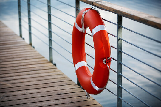 Orange lifebuoy hangs on the railing of a pier near a lake.