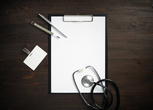 Various medical supplies. Blank medical clipboard, stethoscope, badge, thermometer and pen.