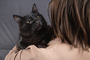 Black cat peeks out from behind a woman's shoulder.