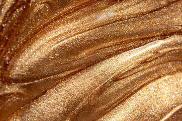 Close up view of golden shimmering cosmetic texture of gel or body spray. Background texture for backdrops or mapping.