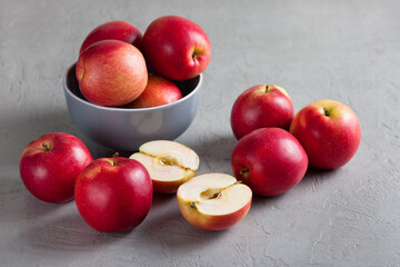A gray ceramic bowl filled with red apples sits on a textured gray surface, with several apples scattered around it. Soft natural light create a calm, minimalist food scene. The concept of healthy