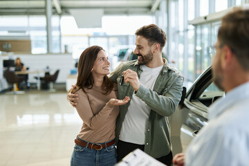 Happy young  couple receiving keys from their new car in a showroom.