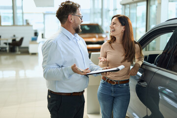 Happy salesman selling the car to his female customer in a showroom. 