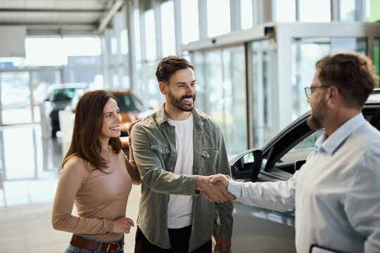 Happy young couple shaking hands with car salesperson in a showroom