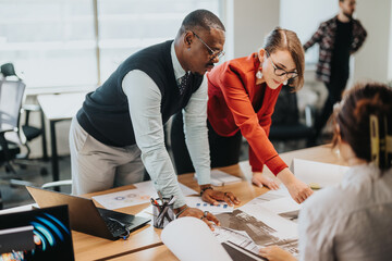 Diverse team of business people engaged in a collaborative project meeting at a busy office. Colleagues are seen discussing and planning with documents and laptops on the table.
