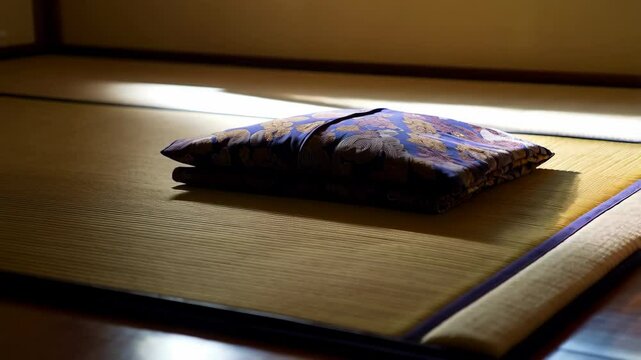 Folded purple futon mattress with floral pattern rests on traditional tatami straw mat flooring in a Japanese interior.