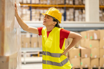 Warehouse worker leaning on pallet, holding her back in pain, indicating possible workplace injury.