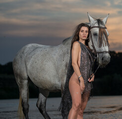 Beautiful brunette woman with long hair and brown scarf  rides  on a white horse in the river....