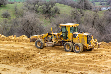 Motor grader on a construction site. Road construction. Leveling the road