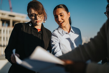 A group of diverse business people working together on a rooftop. The sun is setting, creating a collaborative and innovative atmosphere. The team is focused and engaged, reviewing documents.