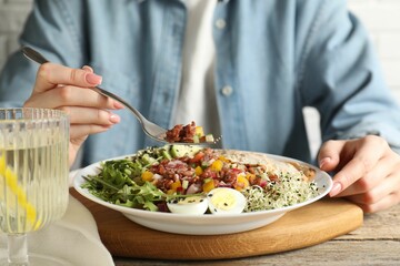 Woman eating delicious salad with brown rice at wooden table, closeup