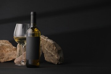Bottle of wine, wineglass and rocks on black background, space for text