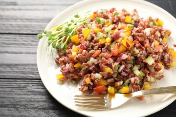Tasty salad with brown rice on black wooden table, closeup