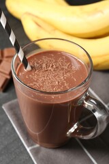 Tasty chocolate milk in glass cup, pieces and bananas on black table, closeup