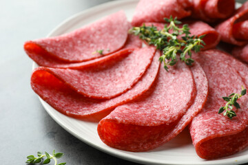 Slices of delicious sausage with thyme served on grey table, closeup