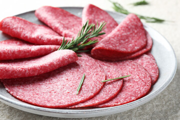 Slices of delicious sausage with rosemary served on white textured table, closeup