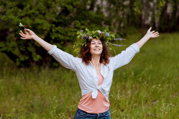 Cheerful adult woman reconnects with summer nature, enjoying the serene countryside. The female model stands in a wildflower wreath during a cultural celebration