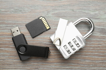 Flash drives, SD memory card and combination padlock on wooden background, flat lay