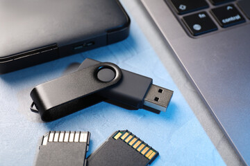 Flash drive, SD memory cards, external hard disk and laptop on light grey table, closeup