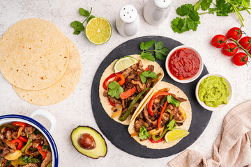 Fajitas, beef meat slices with colored pepper and onions, traditional mexican food, served with tortillas, salsa and sour cream on white background, top view. High quality photo