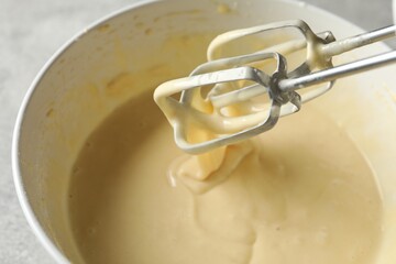 Hand mixer with whisks and bowl of dough on grey table, closeup