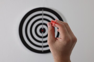 Targeting. Man with arrow aiming at dart board on light background, closeup