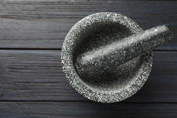 Stone mortar and pestle on black wooden table, top view