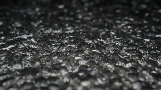 Close-Up View of Dark Metallic Textured Surface with Abstract Bumpy Patterns in Moody Lighting