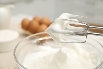 Hand mixer with whisks and bowl of whipped cream on table, closeup