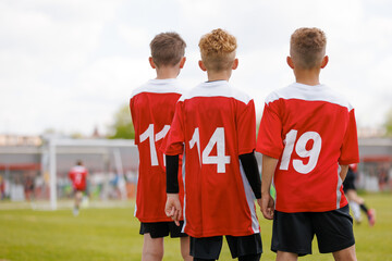 Fototapeta premium Young Boys’ Soccer Team Watching the Game from the Sideline, Wearing Red and White Jerseys at a Youth Tournament