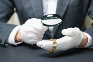 Appraiser evaluating luxury wristwatch at table indoors, closeup