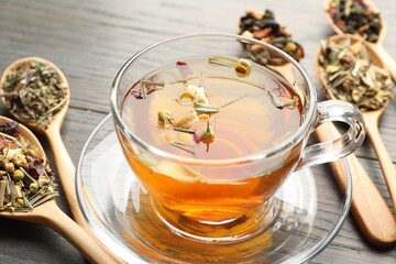 Aromatic herbal tea in glass cup and dry leaves on wooden table, closeup