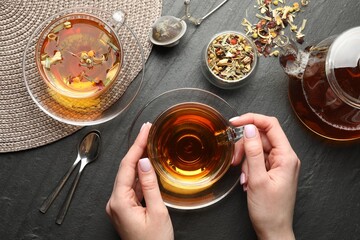Woman with aromatic herbal tea at black table, top view