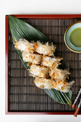 Tuna tataki roll topped with crispy flakes and onions, artfully arranged on a green leaf over a wooden tray.
